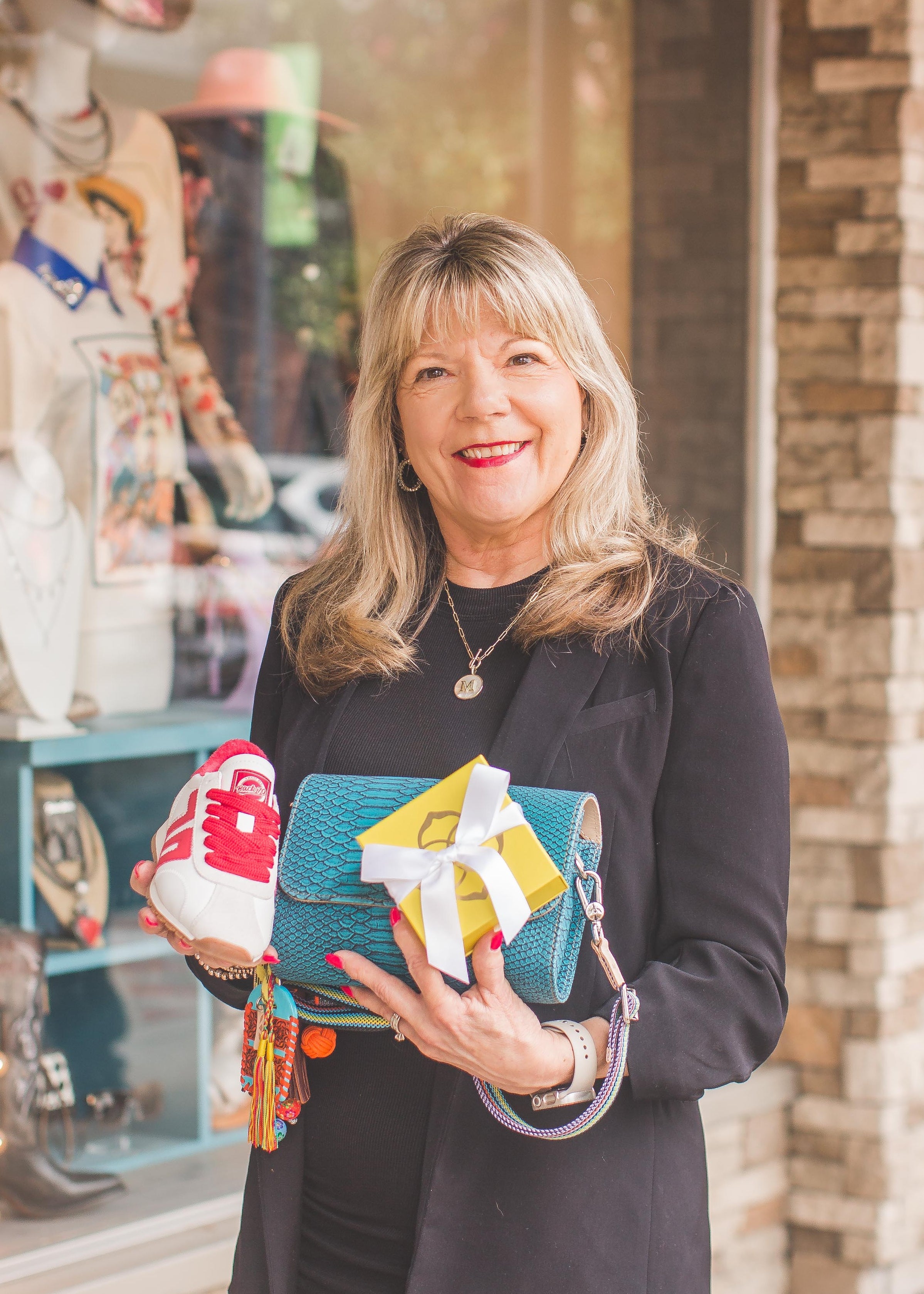 Woman holding colorful bags in front of 'Sass & Class Boutique' with stone facade.